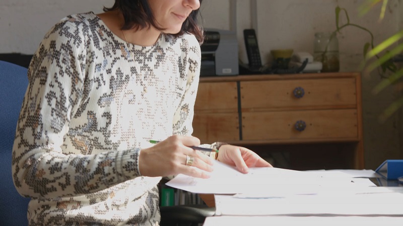 A woman sitting at a desk reviewing documents in a sunlit office