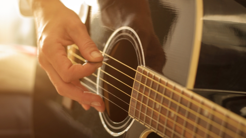 Hand strumming an acoustic guitar near the soundhole, showing a close-up of the strings