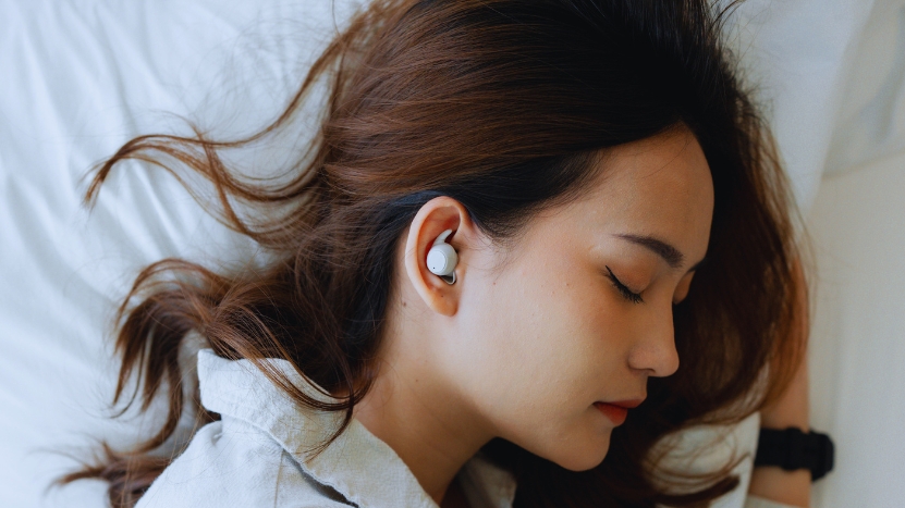 A woman rests on a bed with her eyes closed, showing what it looks like to sleep with earbuds in