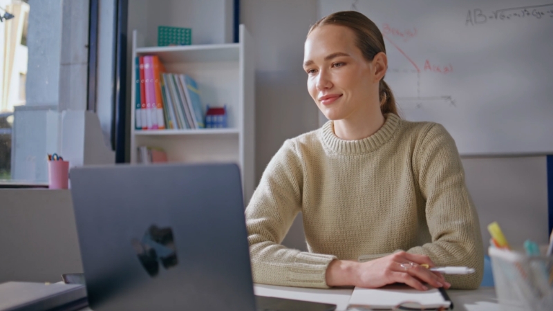 Woman studying on a laptop with notes and equations on a whiteboard, learning math and physics online