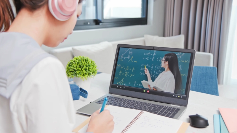 Student watching an online lesson on a laptop and taking notes while learning math and physics