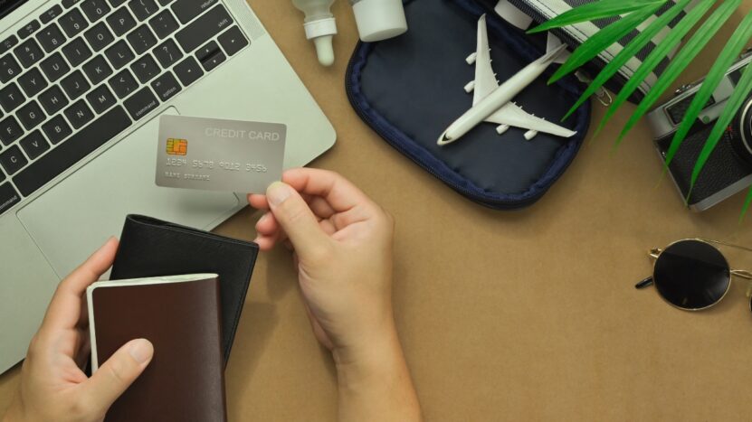 Everyday items for travel sit beside a passport, credit card, laptop, and small airplane model