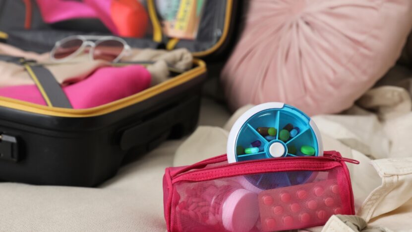 A travel pouch with medicine and toiletries sits beside an open suitcase
